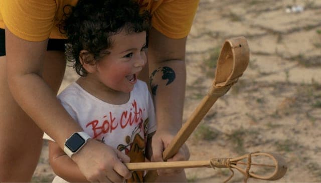 An adult's hands guiding a child holding a tool