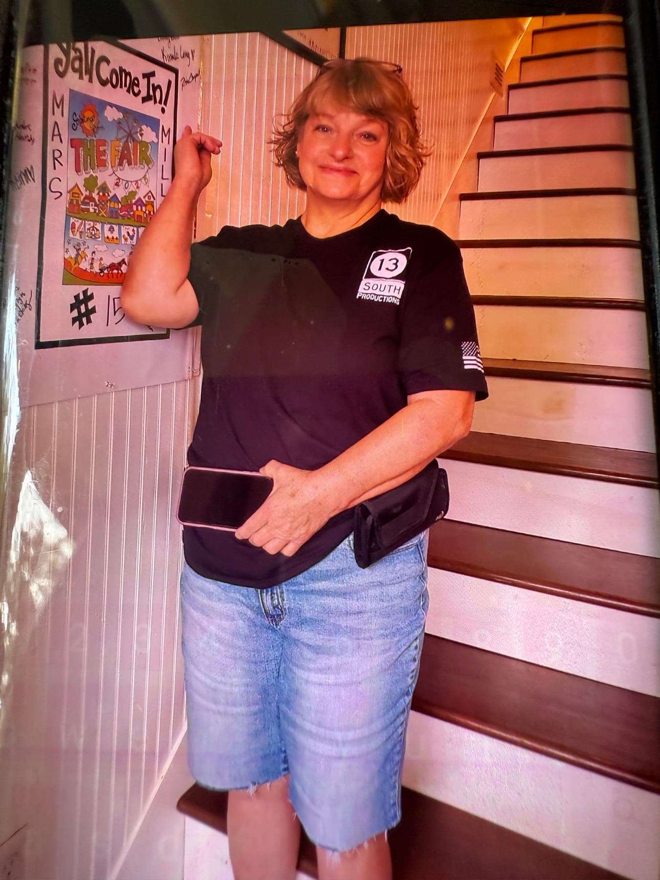 A woman in a 13 South shirt posing beside a staircase