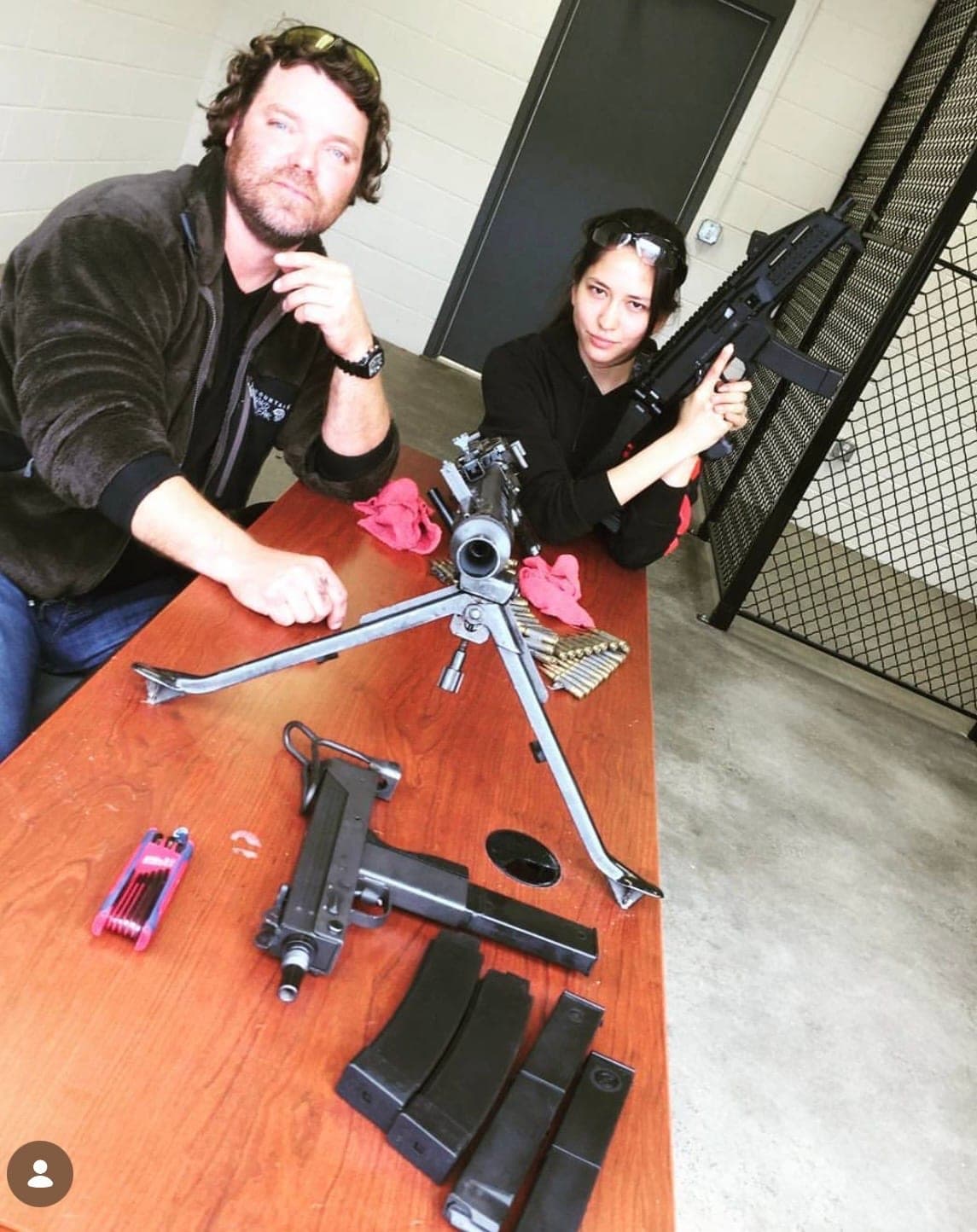 Two people at a table with a disassembled firearm and magazines